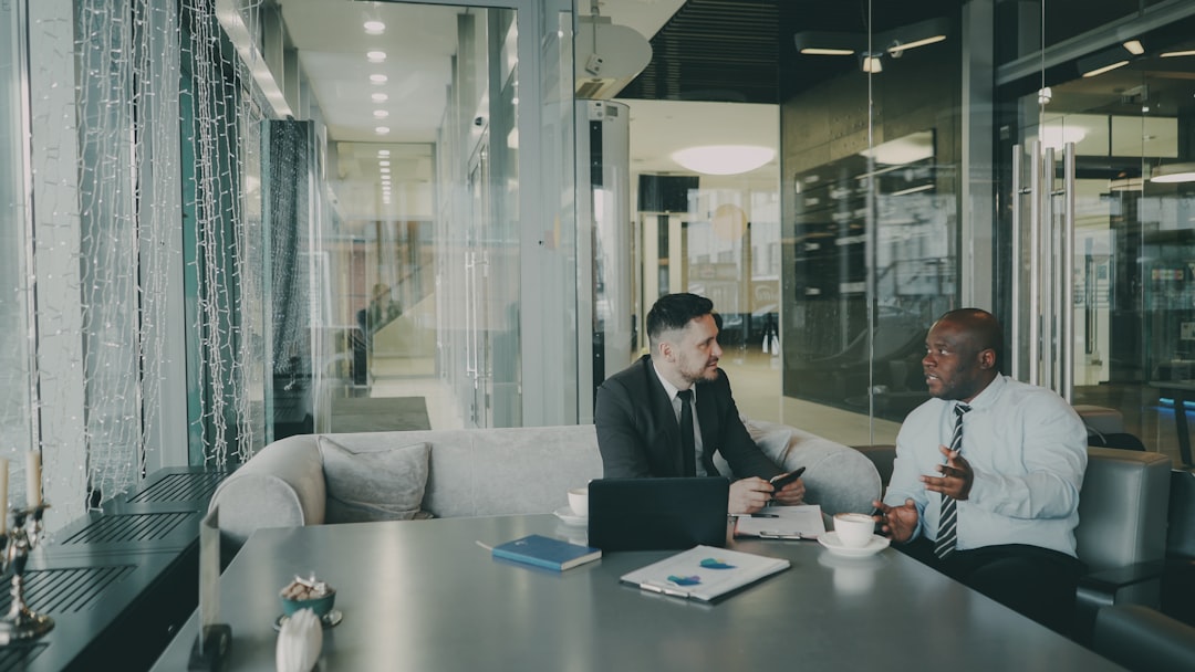 Two optimistic male entrepeneurs in formal clothes discussing their startup project in cafe. African American and Caucasian businessmen talking and sitting at the table with laptop and charts