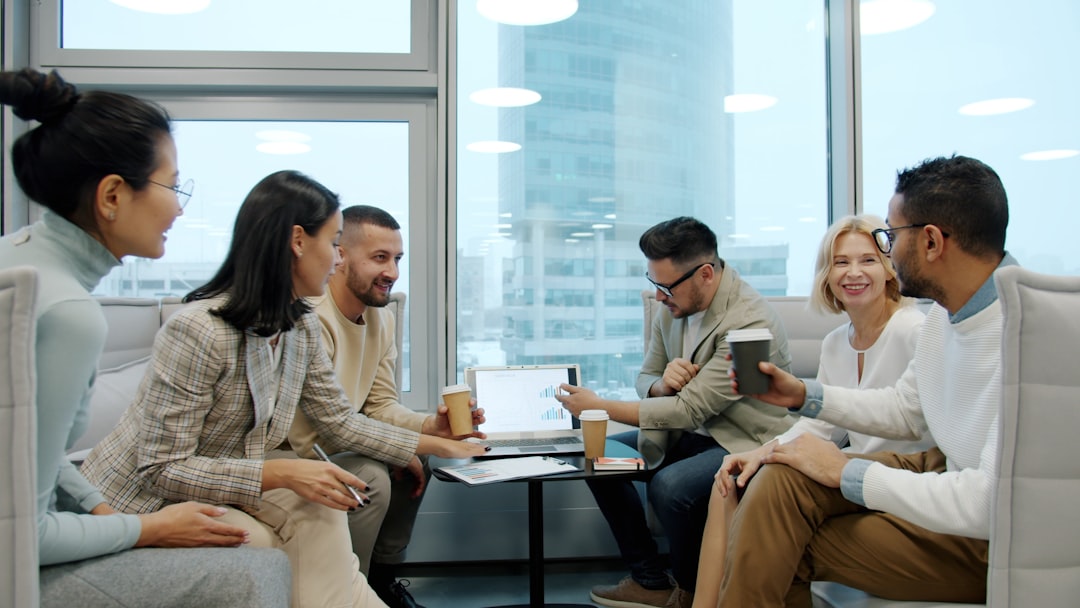 Men and women multiracial team with to go coffee are discussing business in shared office using laptop in office. Communication, people and lifestyle concept.